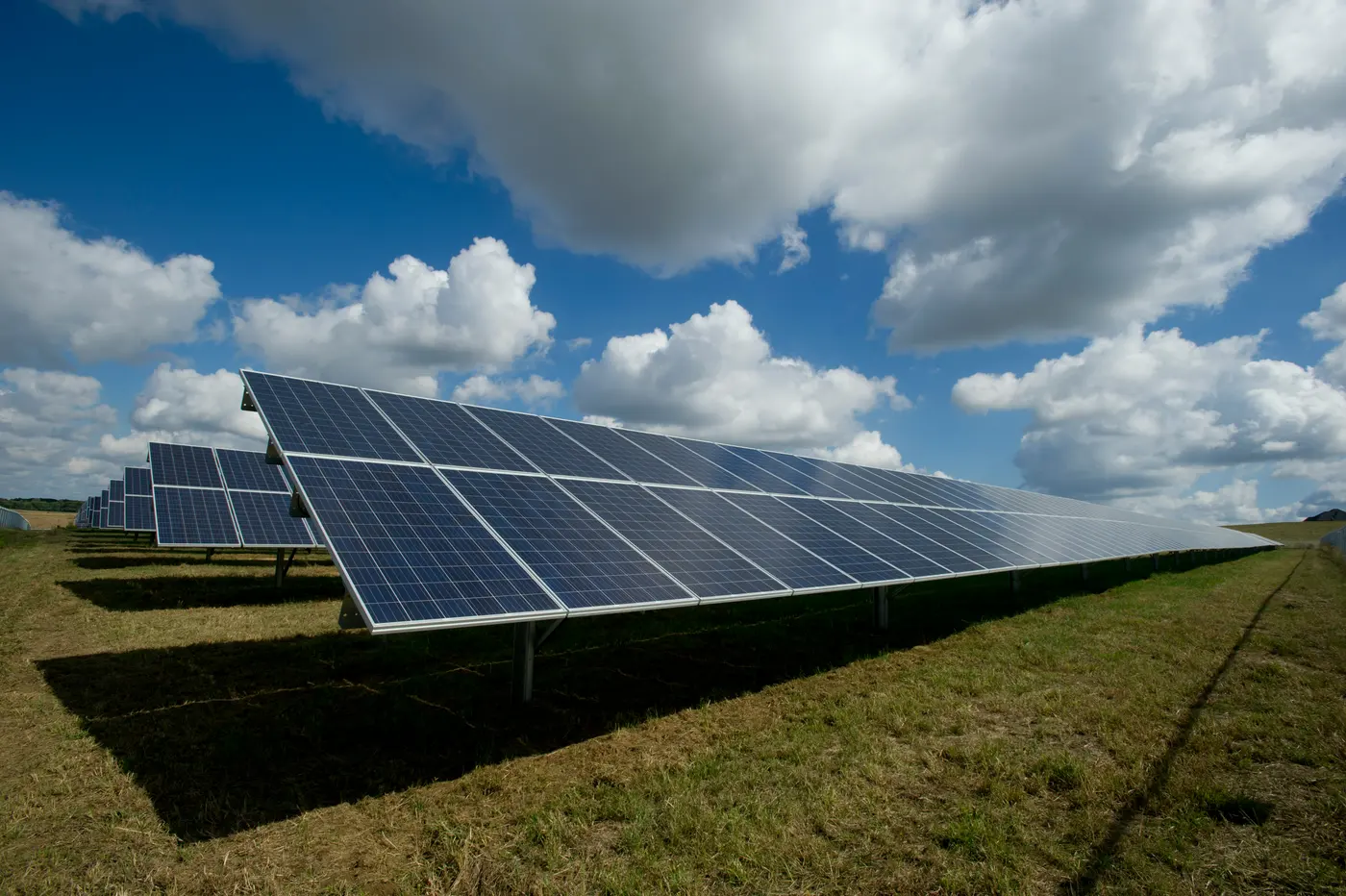 Ground-mounted solar array in a grassy field under a cloudy sky