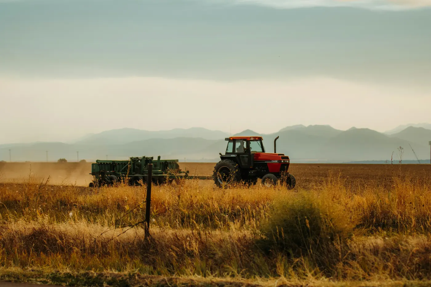 Red tractor pulling a farm trailer across a dry field